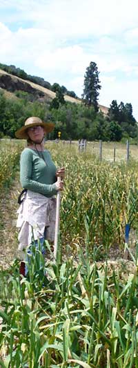 Patty stands with shovel in garlic field by Susan Fluegel at Grey Duck Garlic 